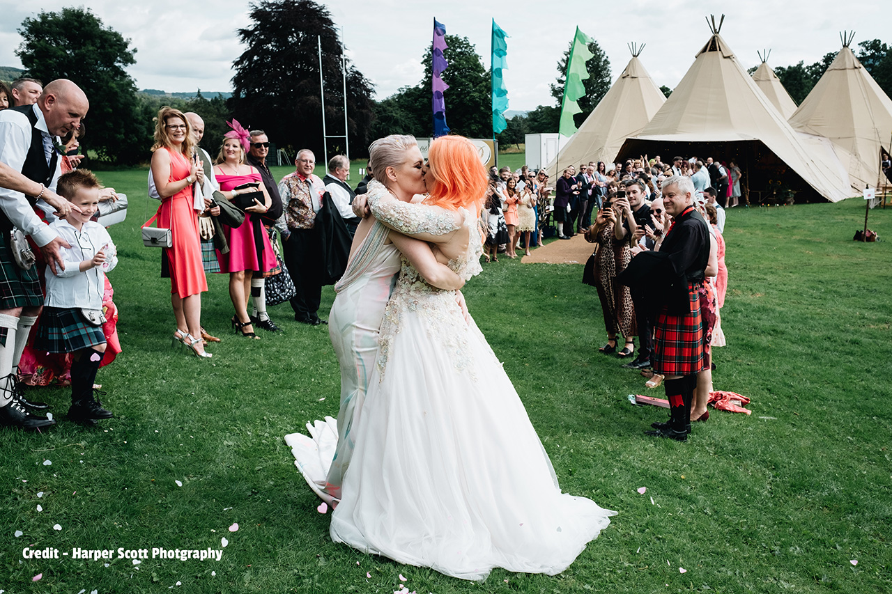 flags for eco wedding couple with bride kissing bride and guests applaud